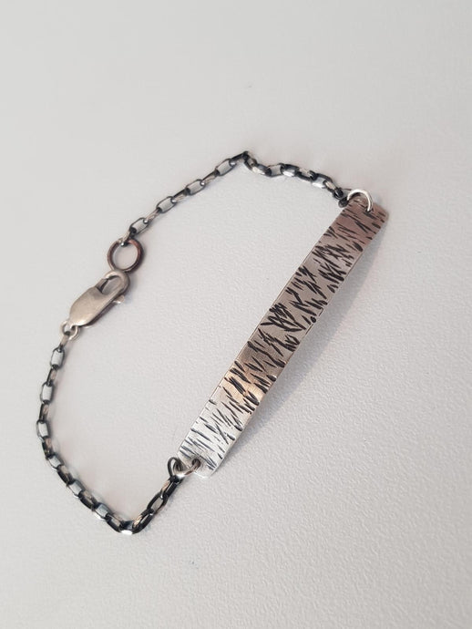 Bracelet with textured metal band and chain on a light gray background