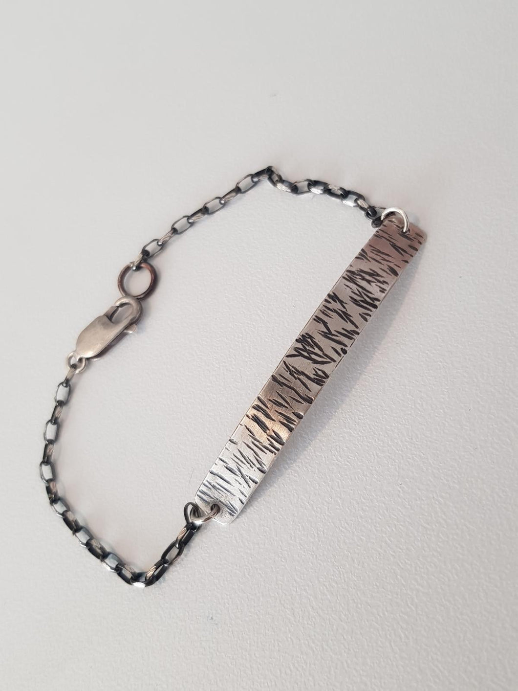Bracelet with textured metal band and chain on a light gray background